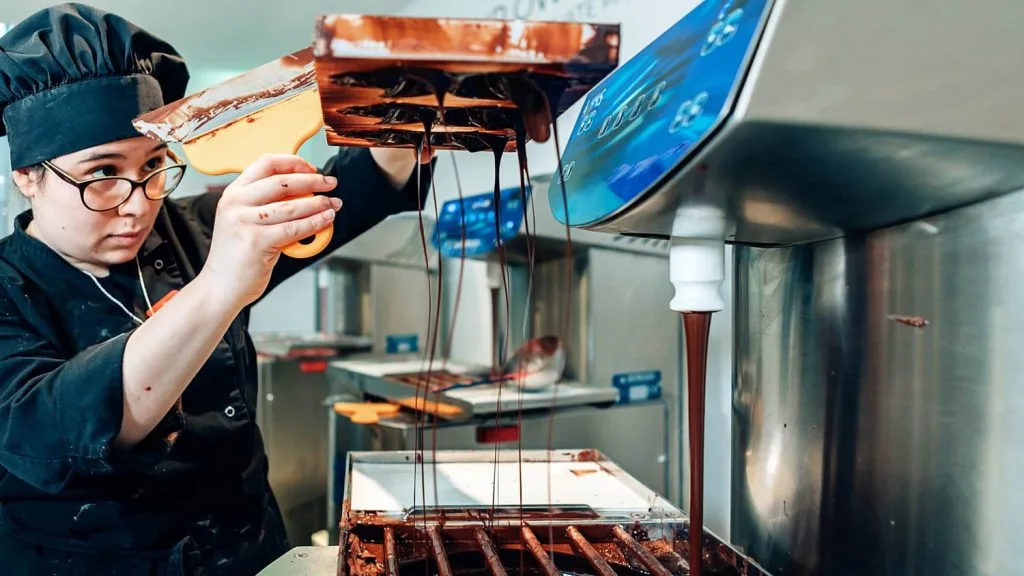 Chocolatière versant du chocolat tempéré sur une grille